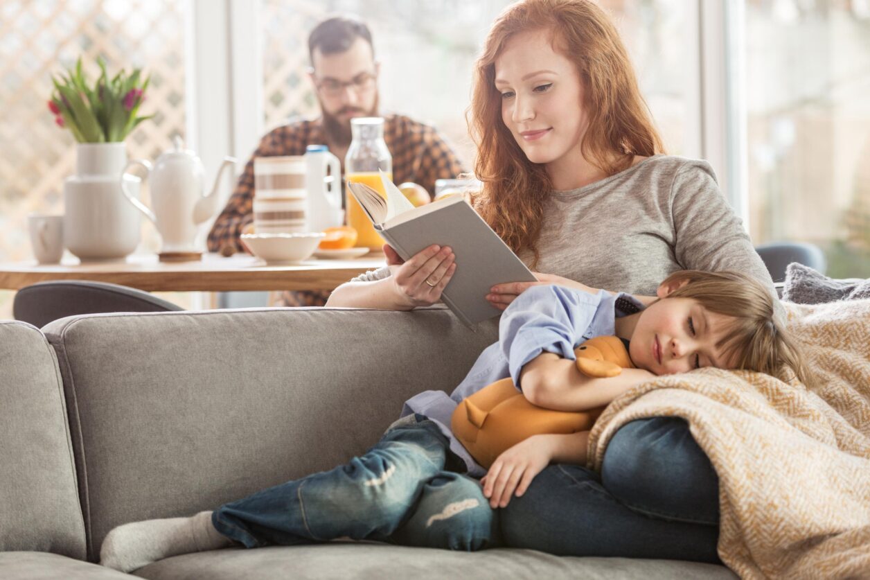woman reading on couch with child sleeping in her lap