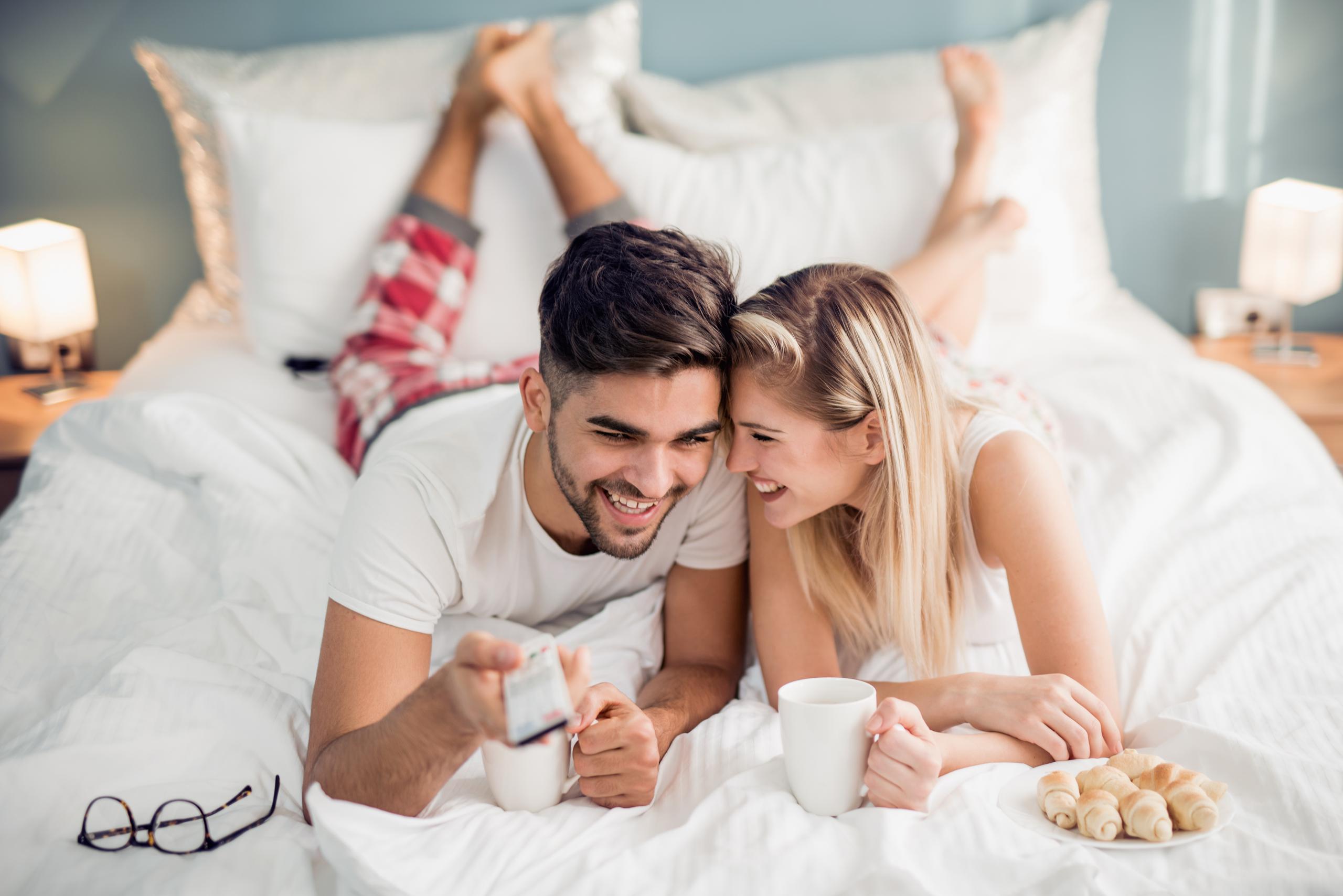 young couple watching television in bed and laughing