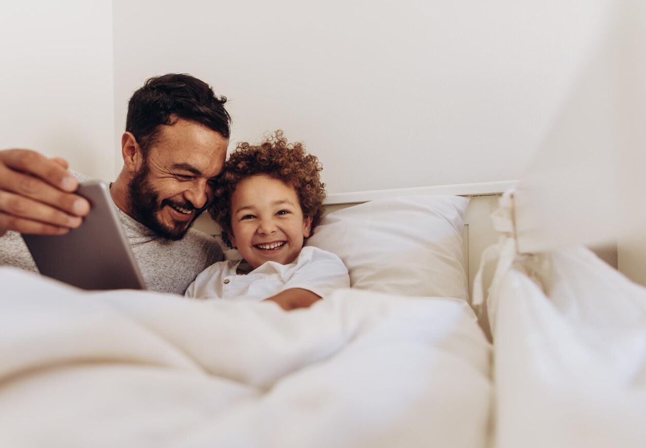 father laughing with child while in bed