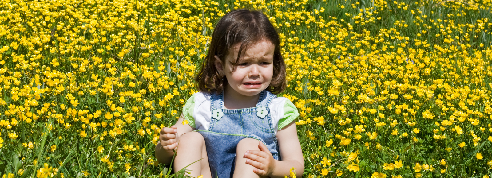 Crying girl sitting on a meadow full of buttercup