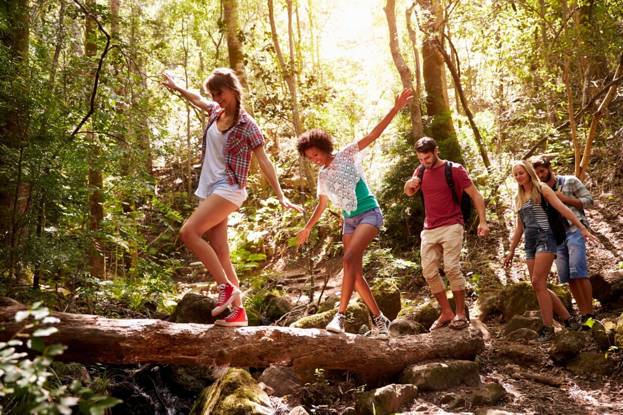 young adults crossing a log in the woods