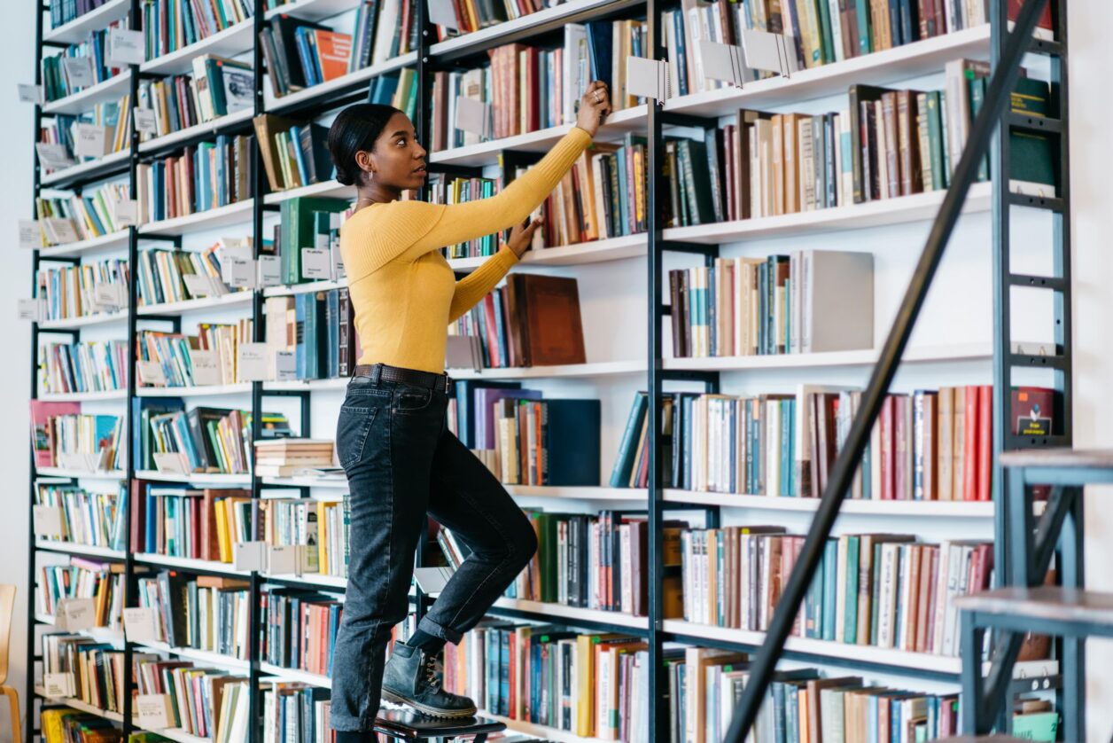 young woman on ladder putting a book on the shelf